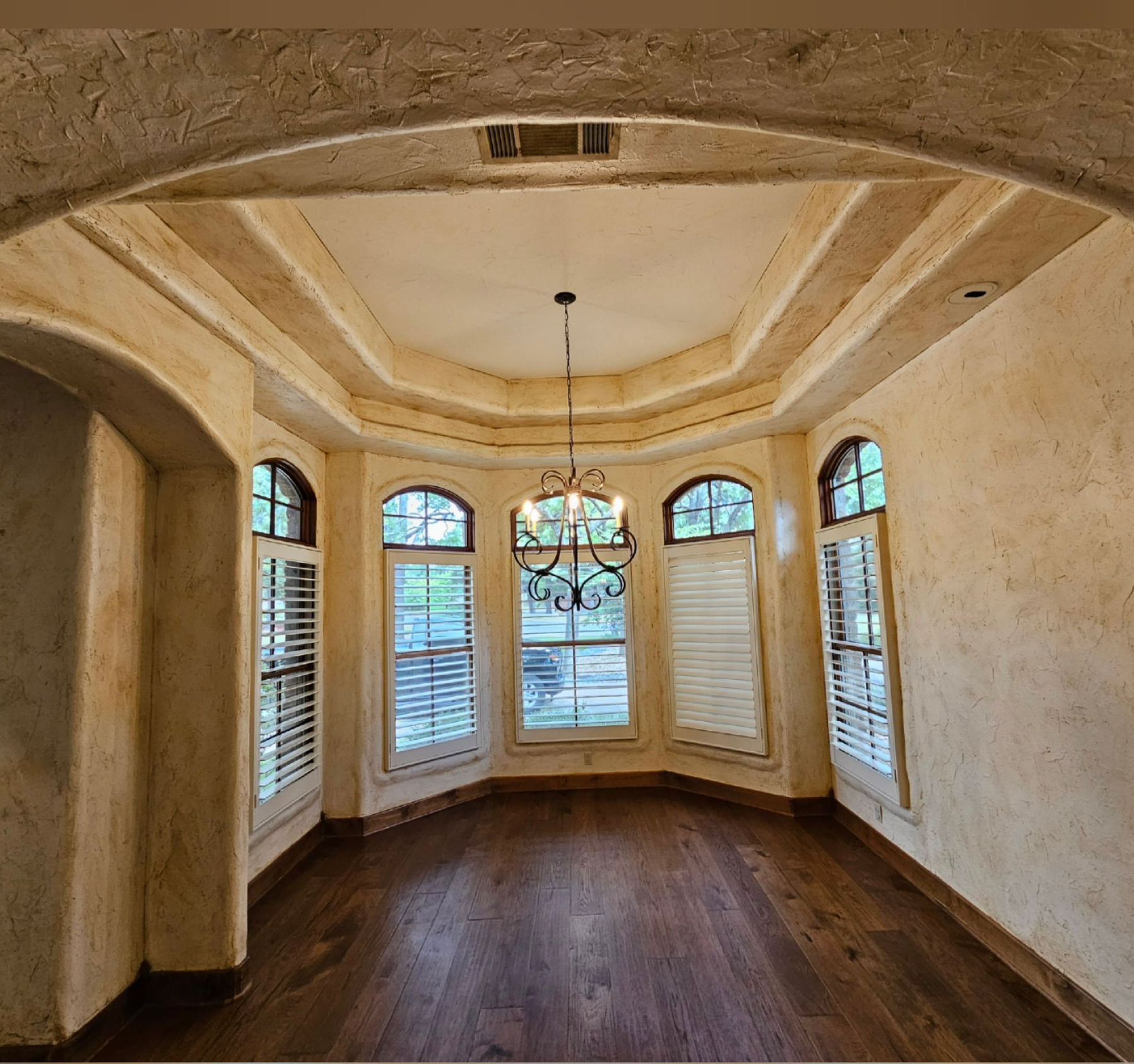 Empty elegant dining room with arched windows, wood floors, and a chandelier