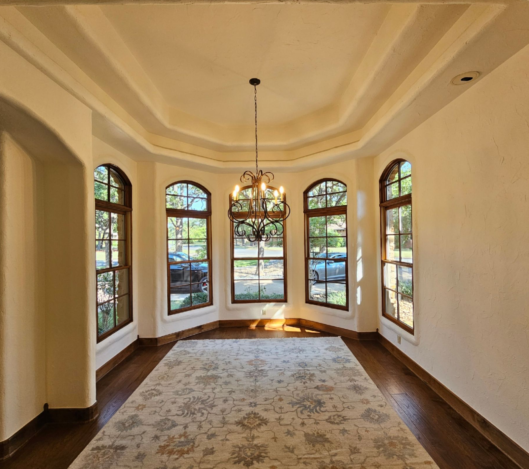 Elegant empty room with arched windows, chandelier, and patterned rug in warm daylight