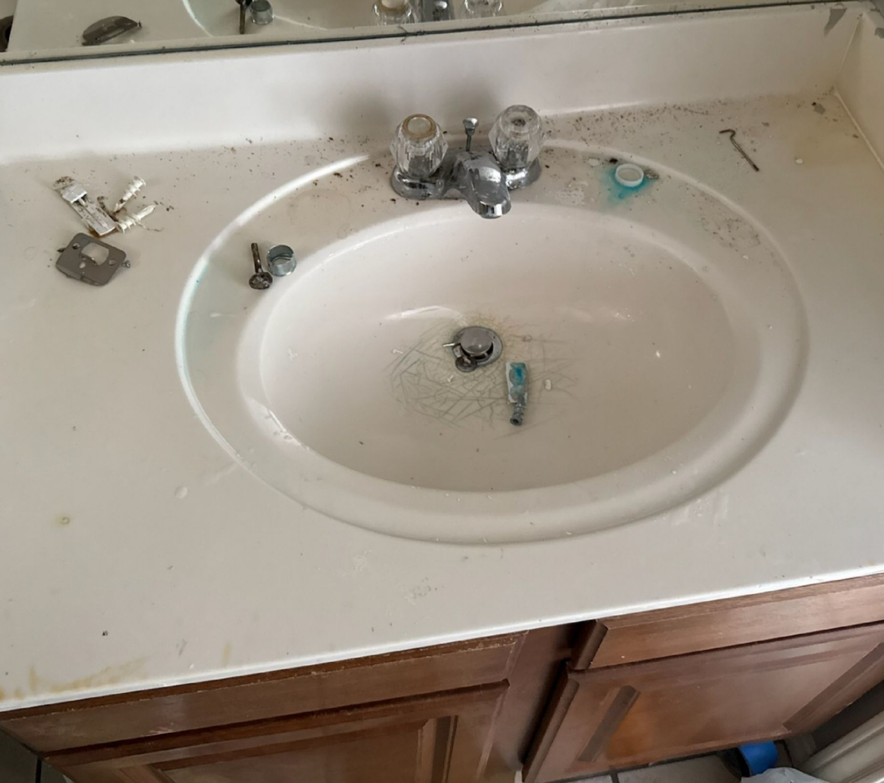Damaged bathroom sink countertop with missing faucet parts and scattered debris