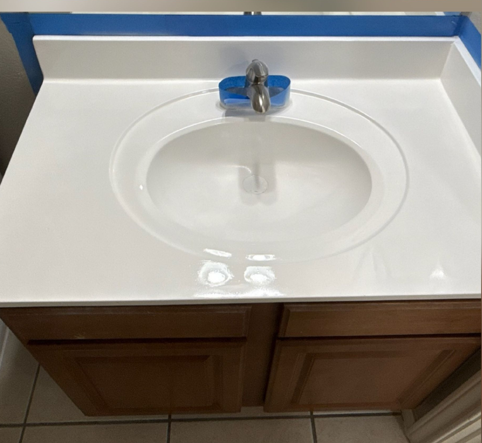 White bathroom sink and counter with blue painter’s tape along the backsplash.