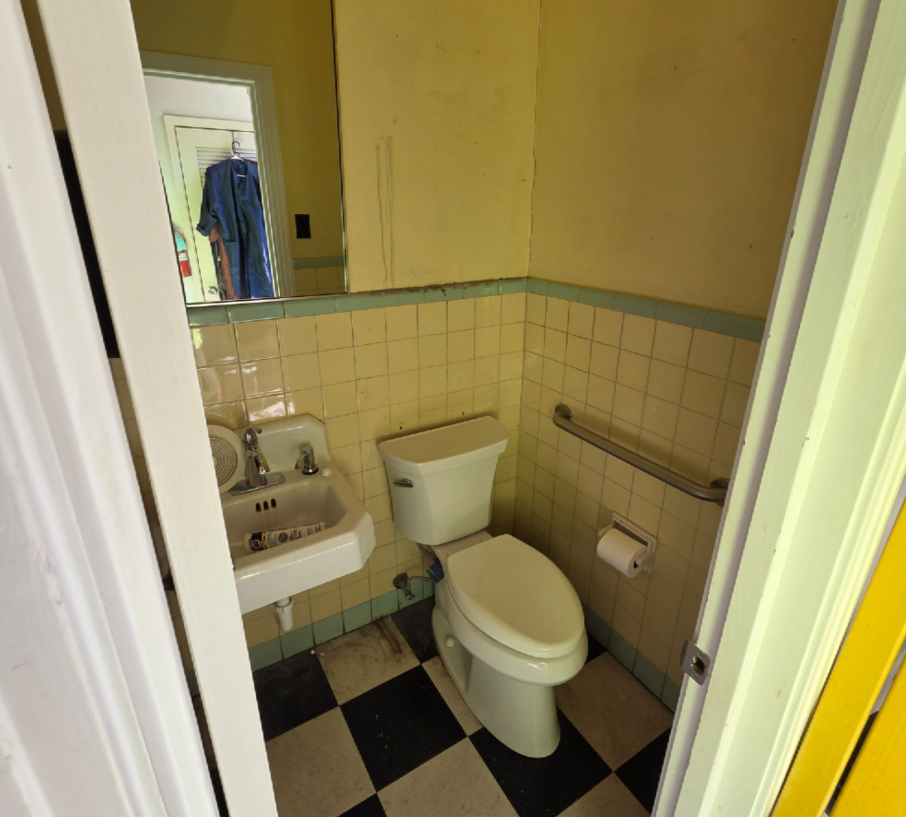 Small bathroom with toilet, sink, beige tiles, black-and-white floor, and a grab bar.