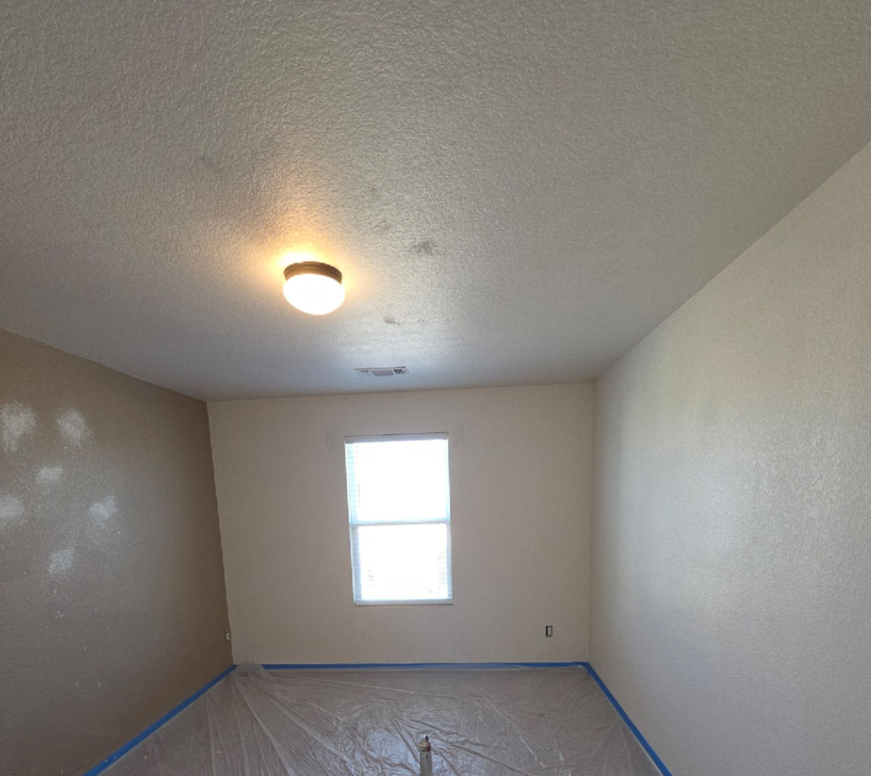 Empty room with beige walls, a small window, and covered floor under a ceiling light.