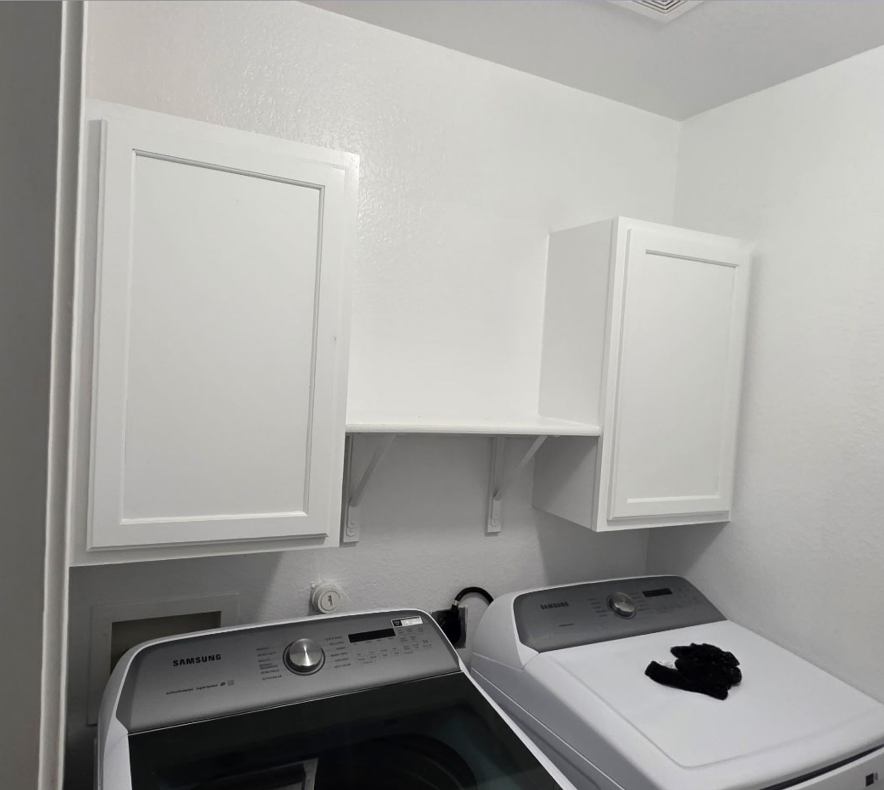 Laundry room with white cabinets above a washer and dryer, and a black cat resting on the dryer lid