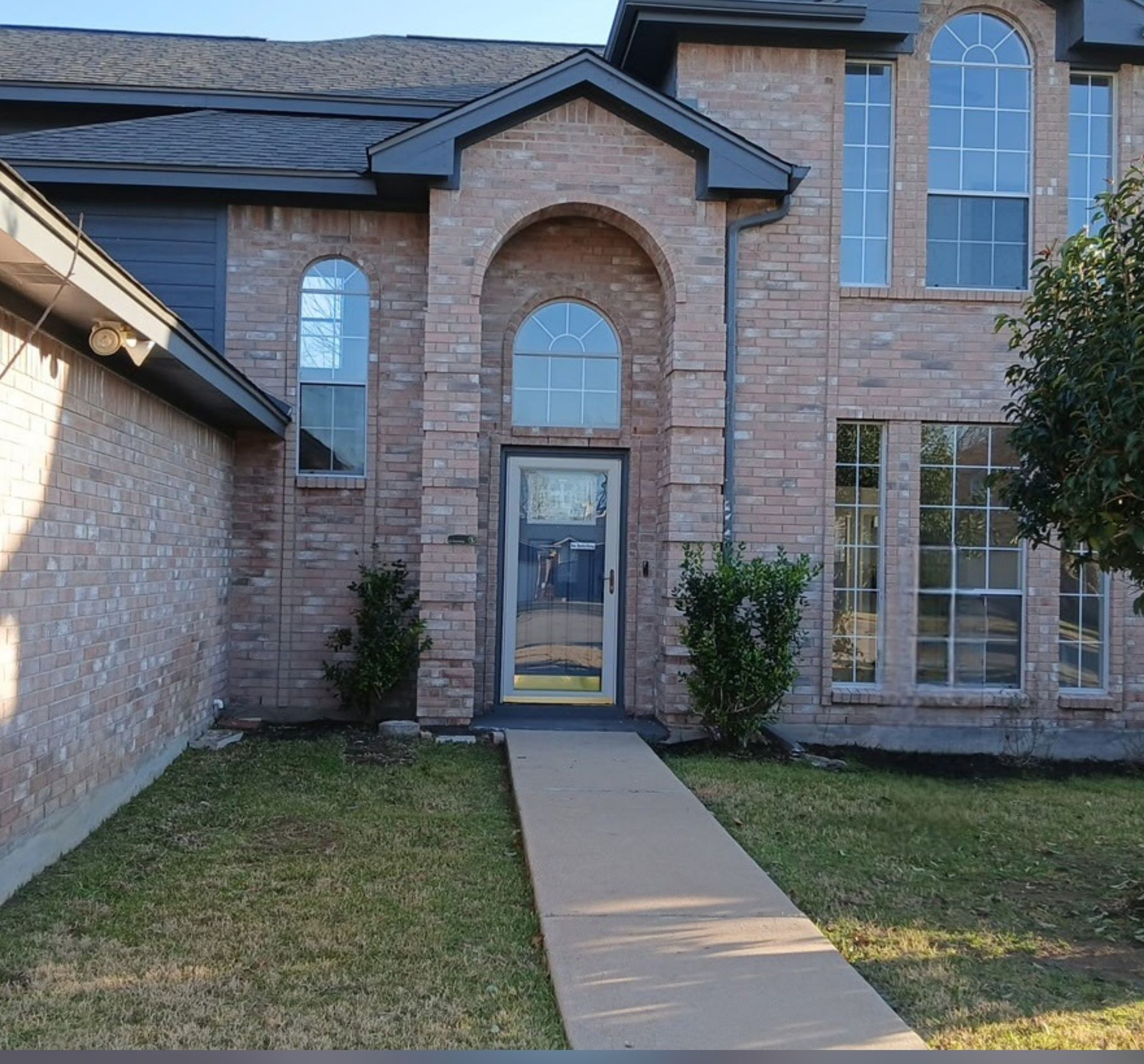 Front view of a brick house with a centered walkway leading to the glass front door.