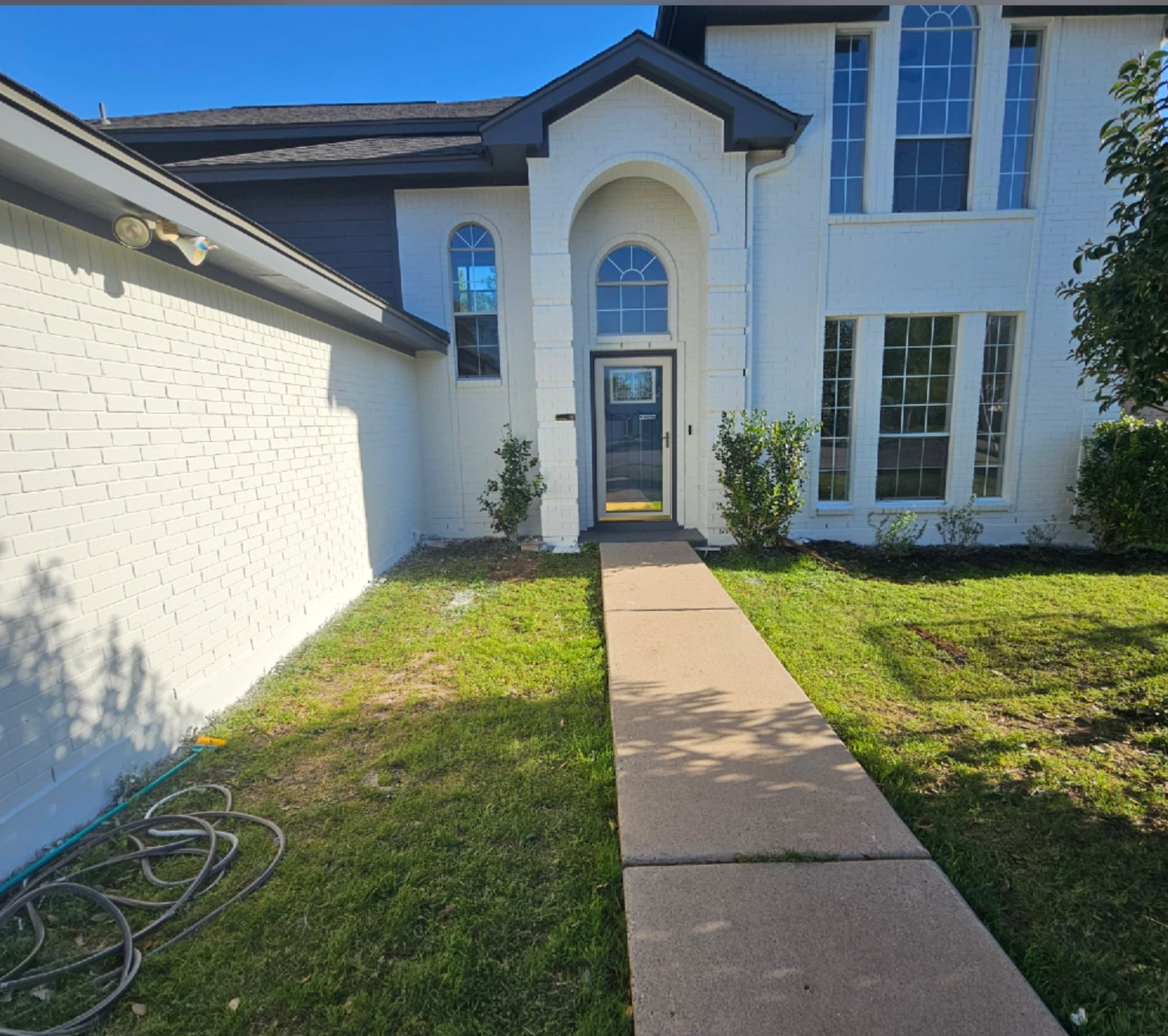 Front walkway leading to a white two-story house with arched entry and green lawn