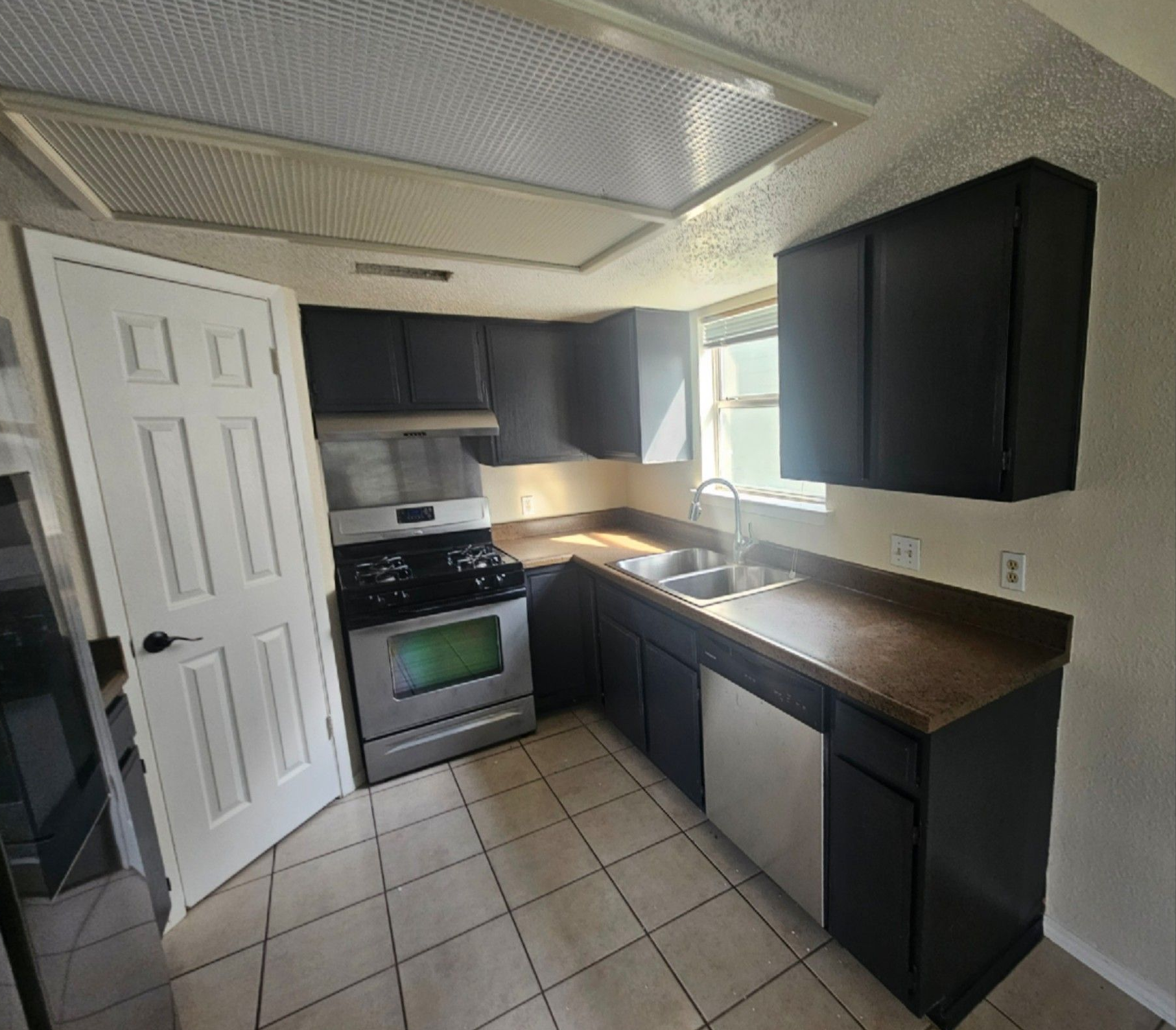 Empty wall with a small white shelf, electrical outlet, and patterned tile on the right; slight wall staining.