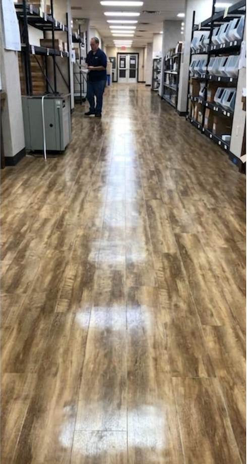 Long indoor hallway with wood-look flooring and shelves on both sides; one person stands in the distance