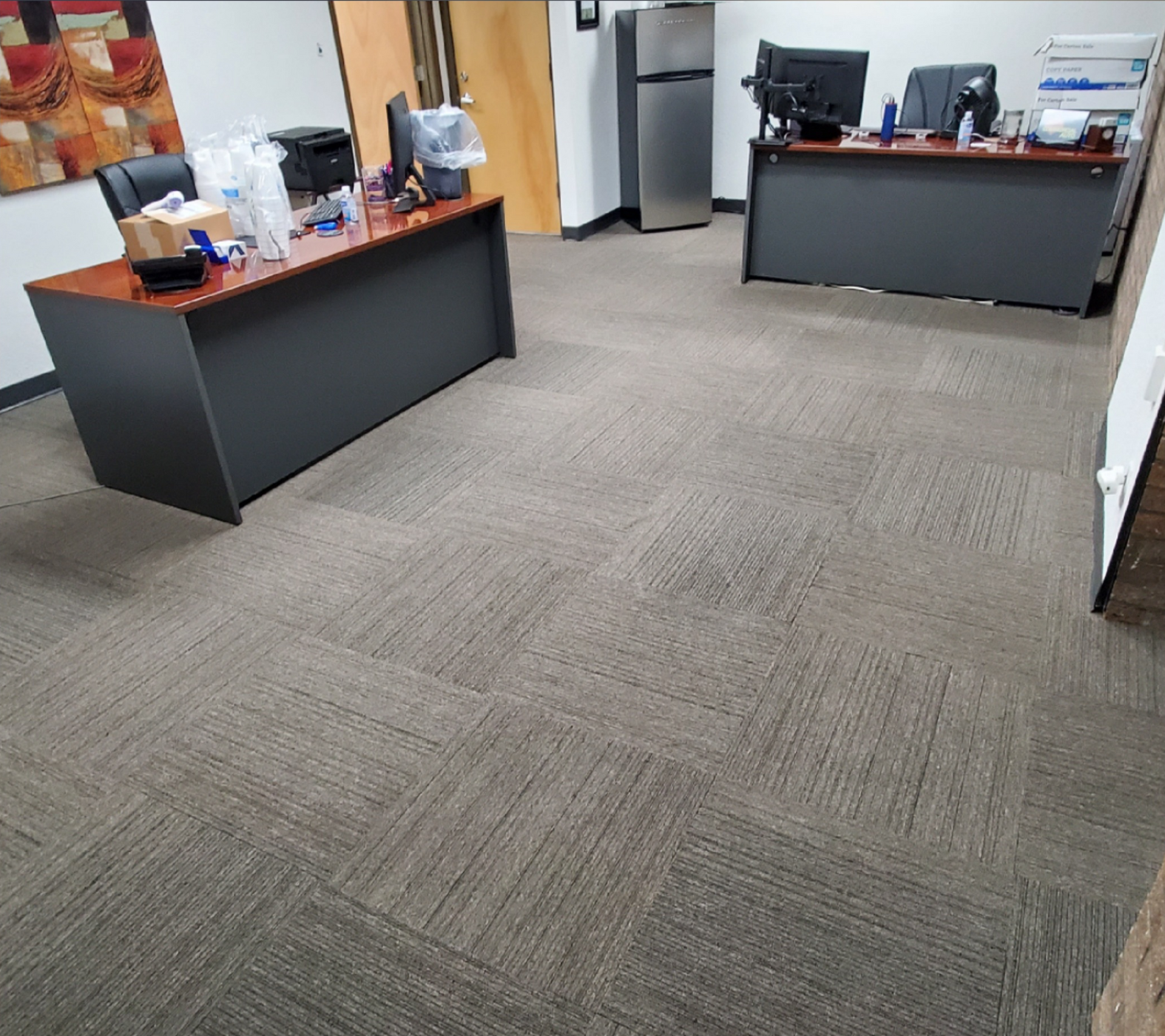 Empty office with two desks, chairs, and a gray carpeted floor.