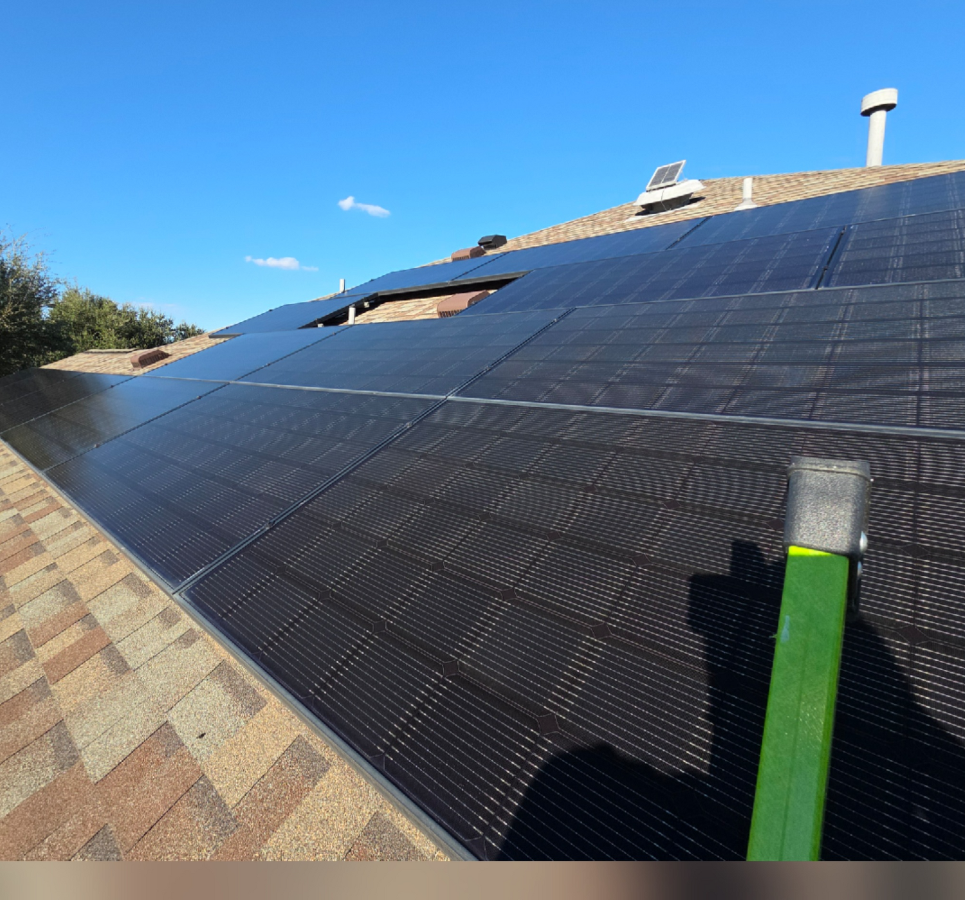 Roof covered with black solar panels under a clear blue sky, with a chimney and vent visible.
