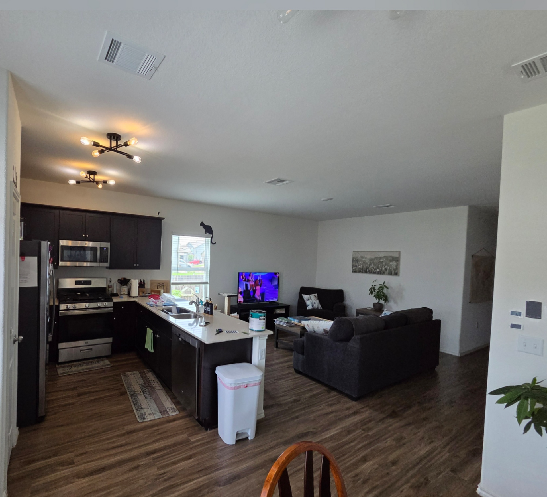 Open-plan living room and kitchen with dark cabinets, gray couch, TV, and wood-look flooring