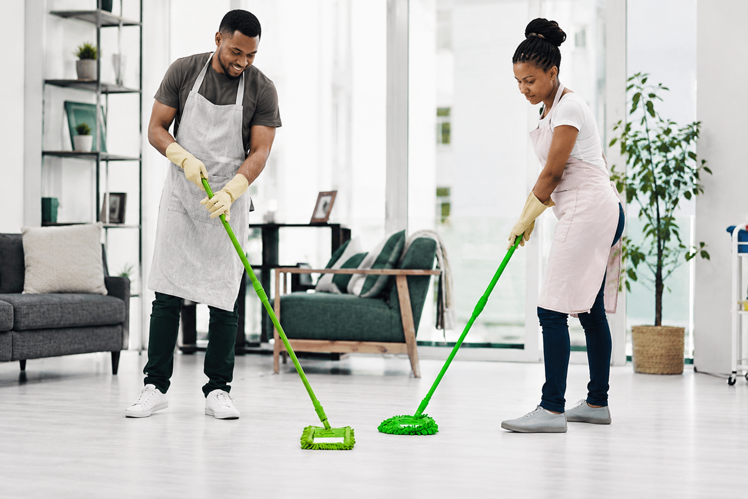 Two people mopping a bright living room floor with green mop heads.