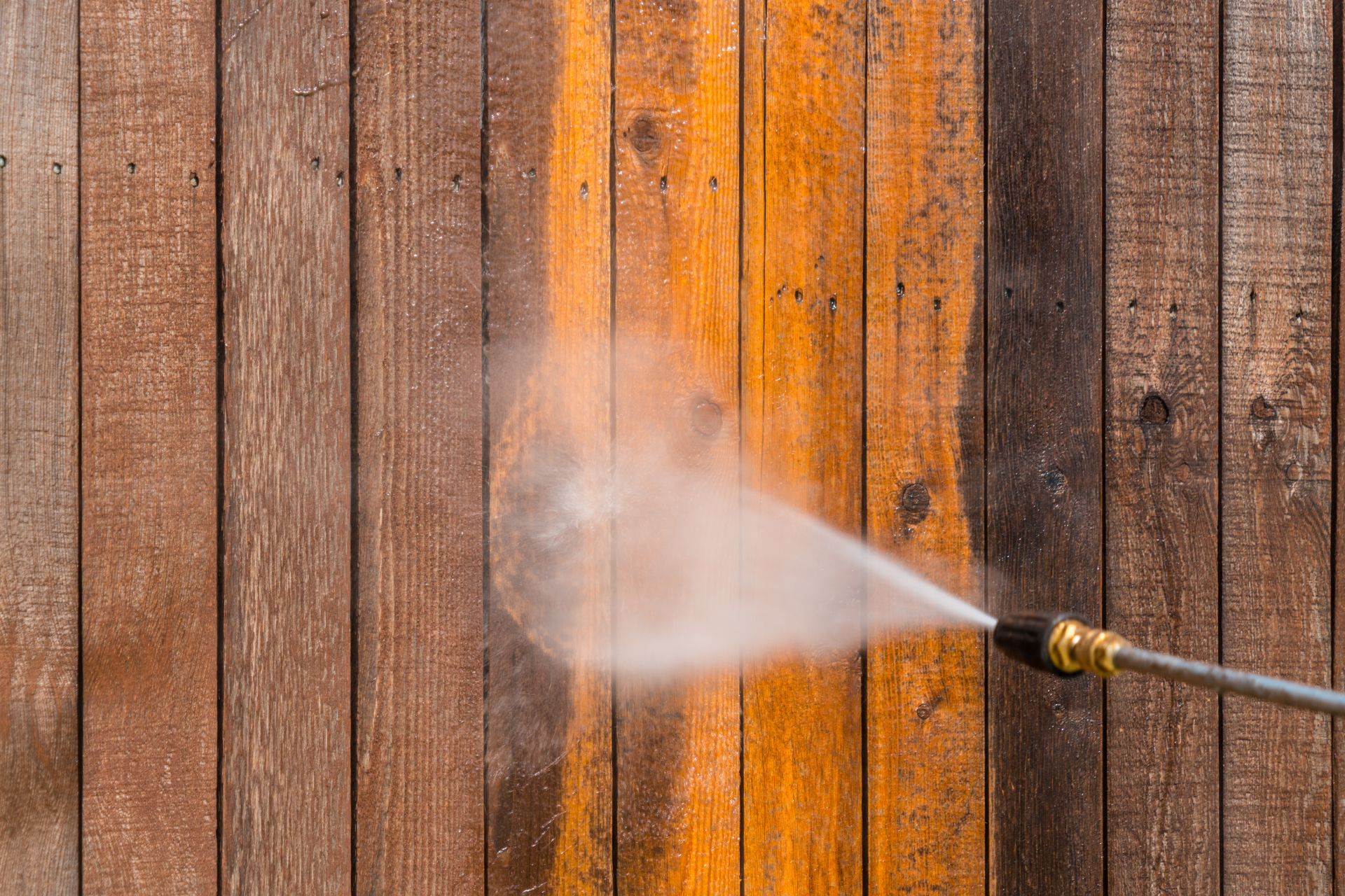 Pressure washer spraying a wooden fence, removing dirt from orange-stained boards
