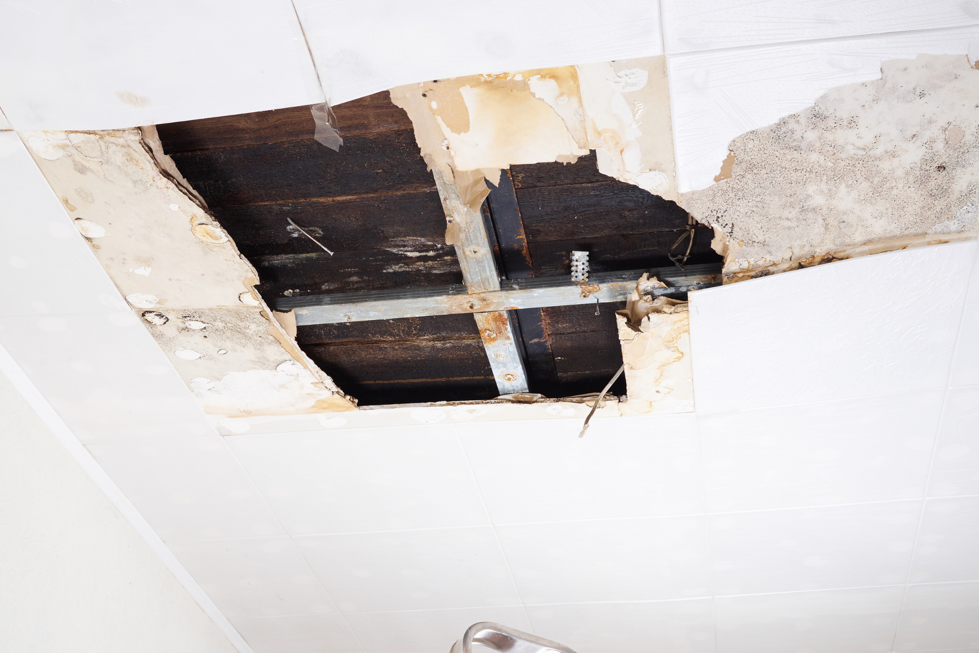 Damaged ceiling with a large hole exposing dark beams and peeling plaster