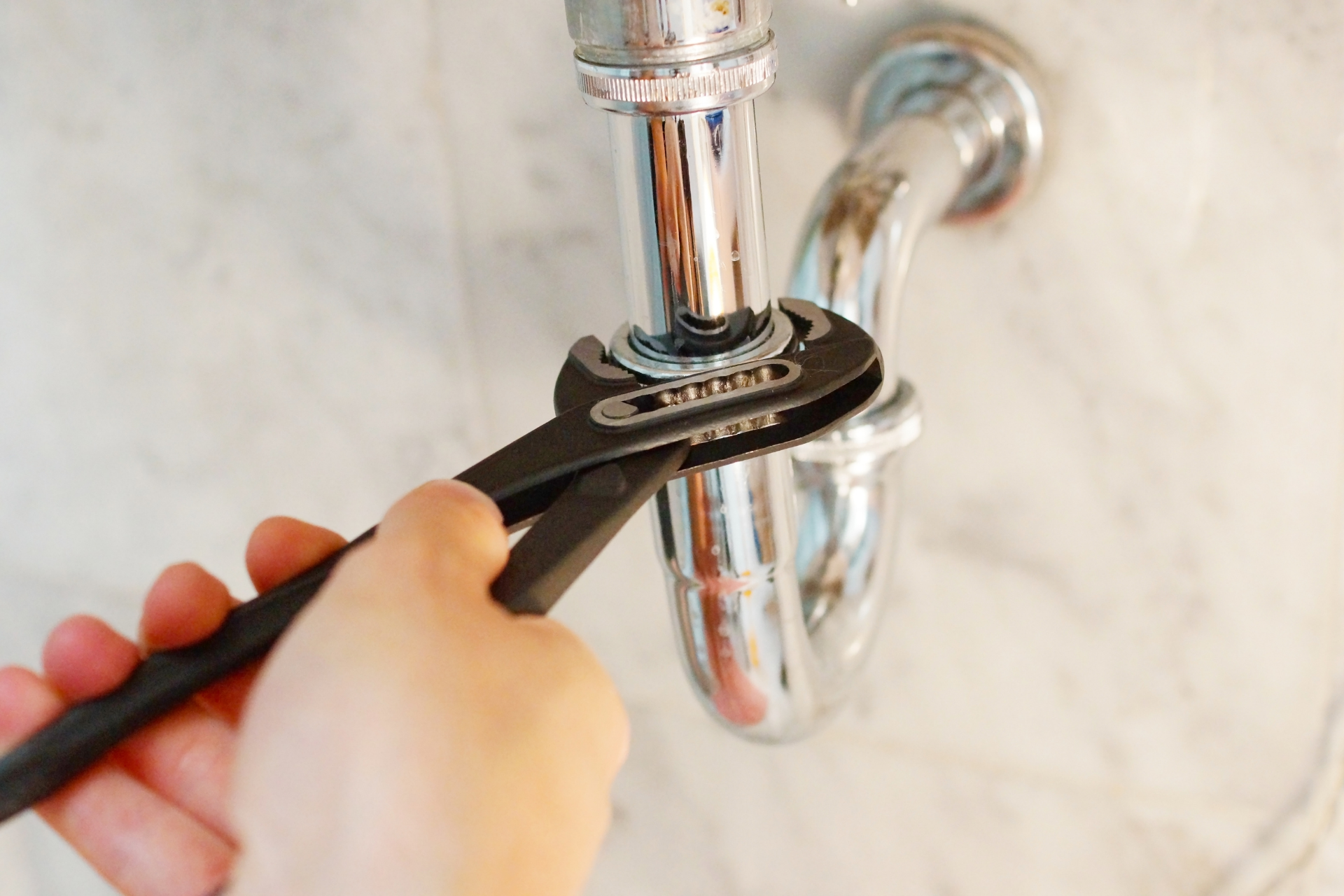 Hand using a wrench to tighten a pipe under a bathroom sink