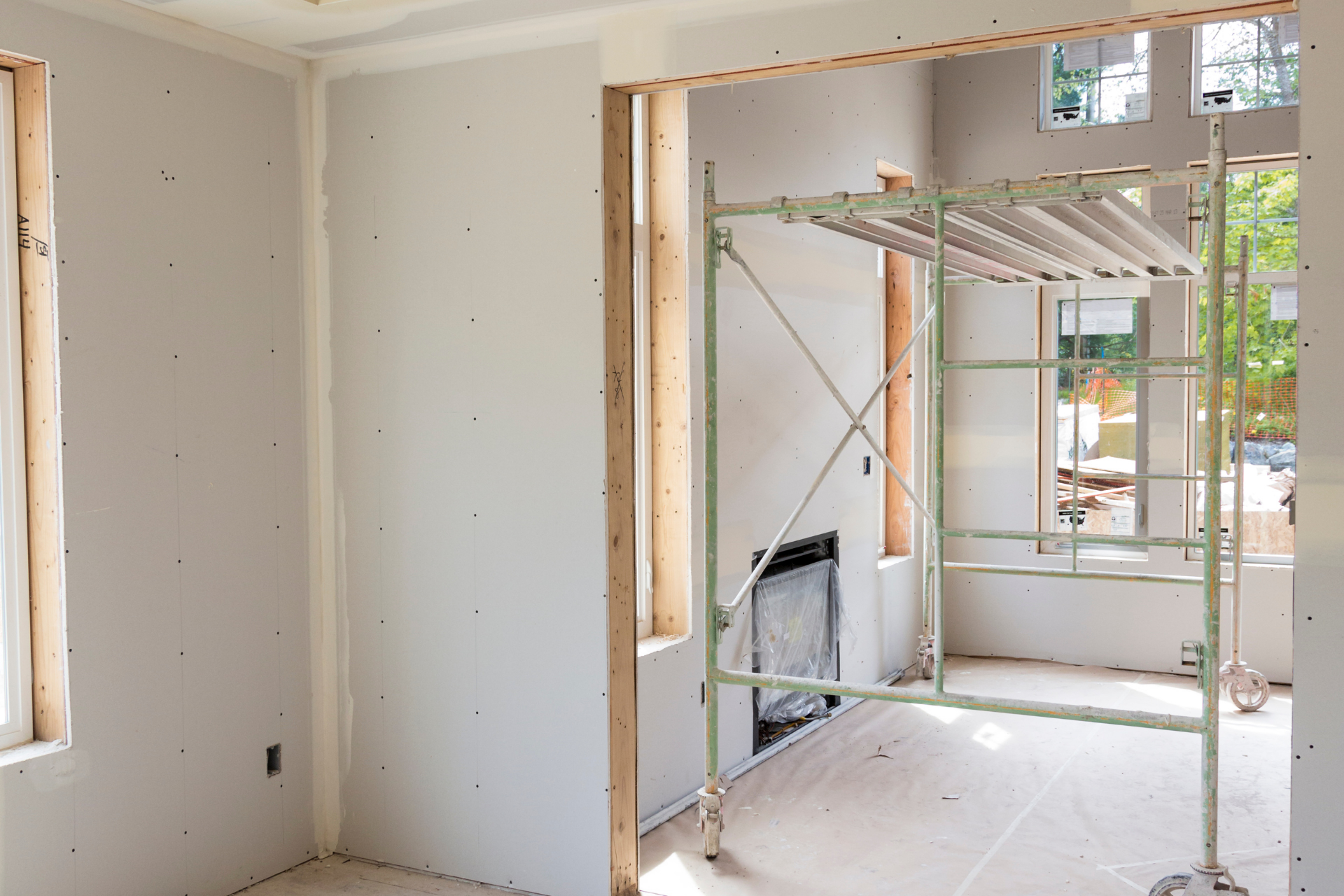 Interior room under renovation with drywall, scaffolding, and unfinished windows