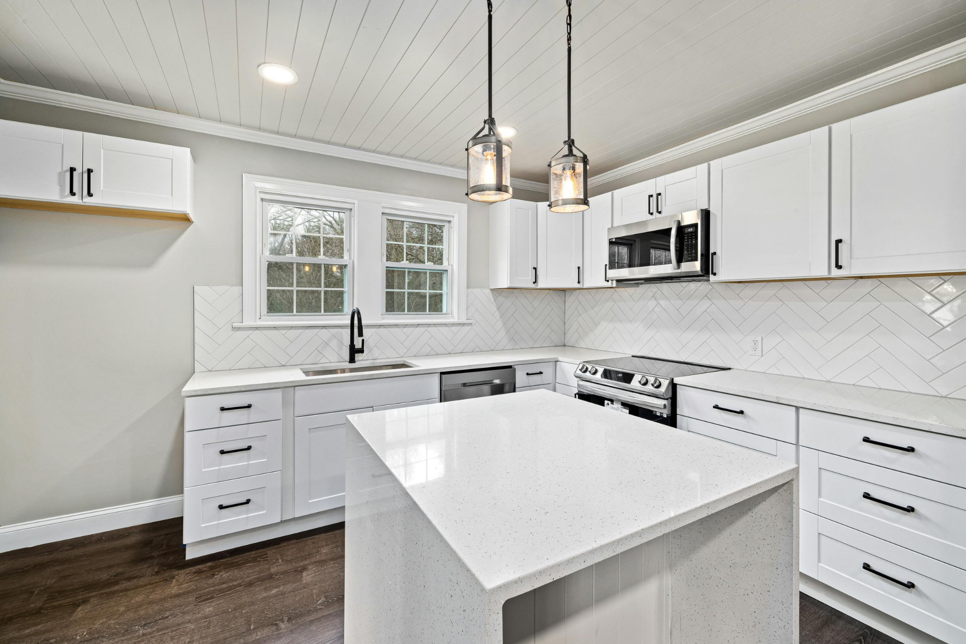 Bright white modern kitchen with island, stainless appliances, and pendant lights