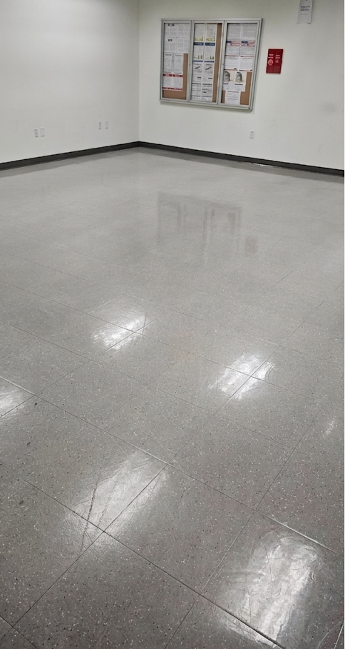 Empty room with glossy gray floor, white walls, and a bulletin board on the far wall.