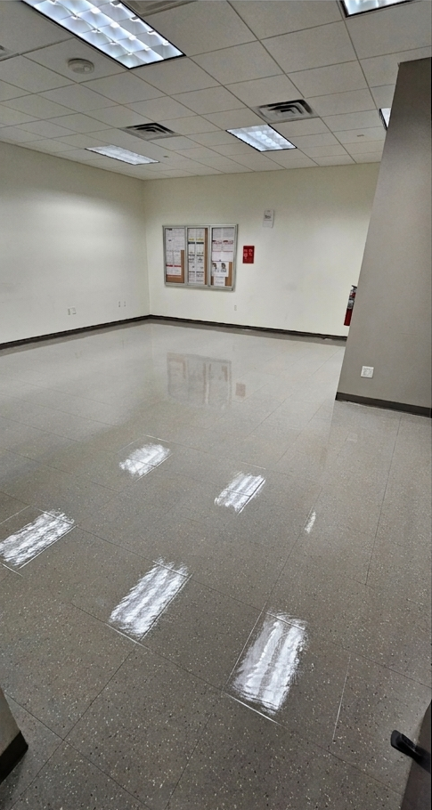 Empty beige office room with glossy tile floor, ceiling lights, and bulletin boards on the far wall
