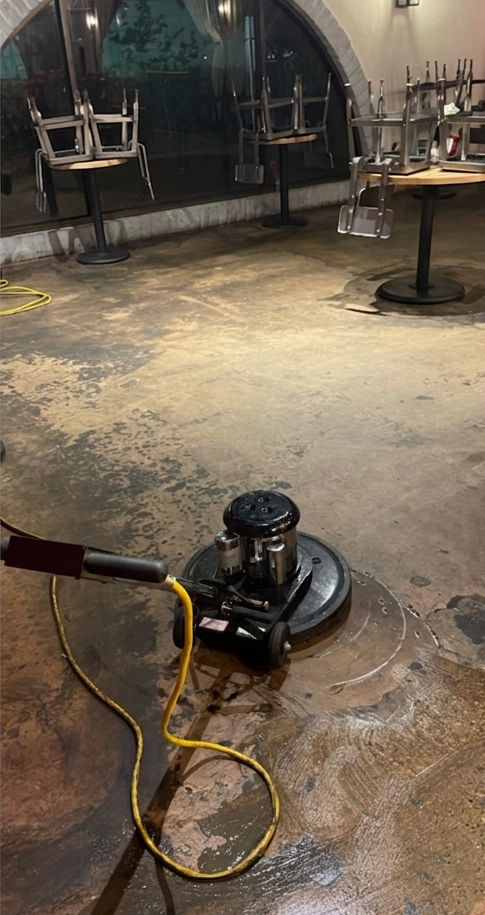 Floor buffer machine on a worn concrete floor in an empty room with tables and chairs in the background