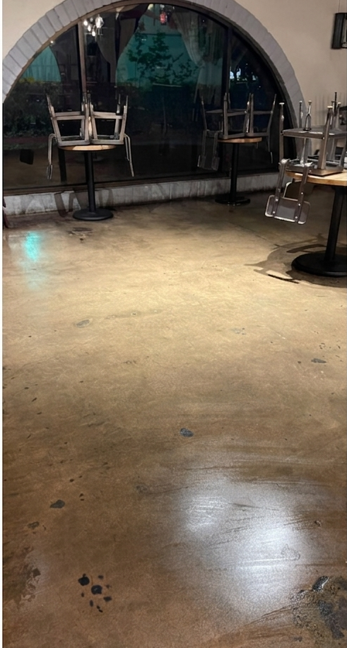 Empty indoor room with polished concrete floor, arched window, and stacked tables and chairs along the walls