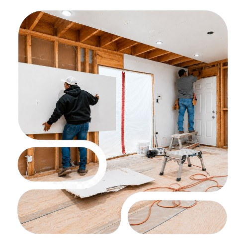 Two workers framing and drywalling a room during interior renovation, with ladders and tools visible.
