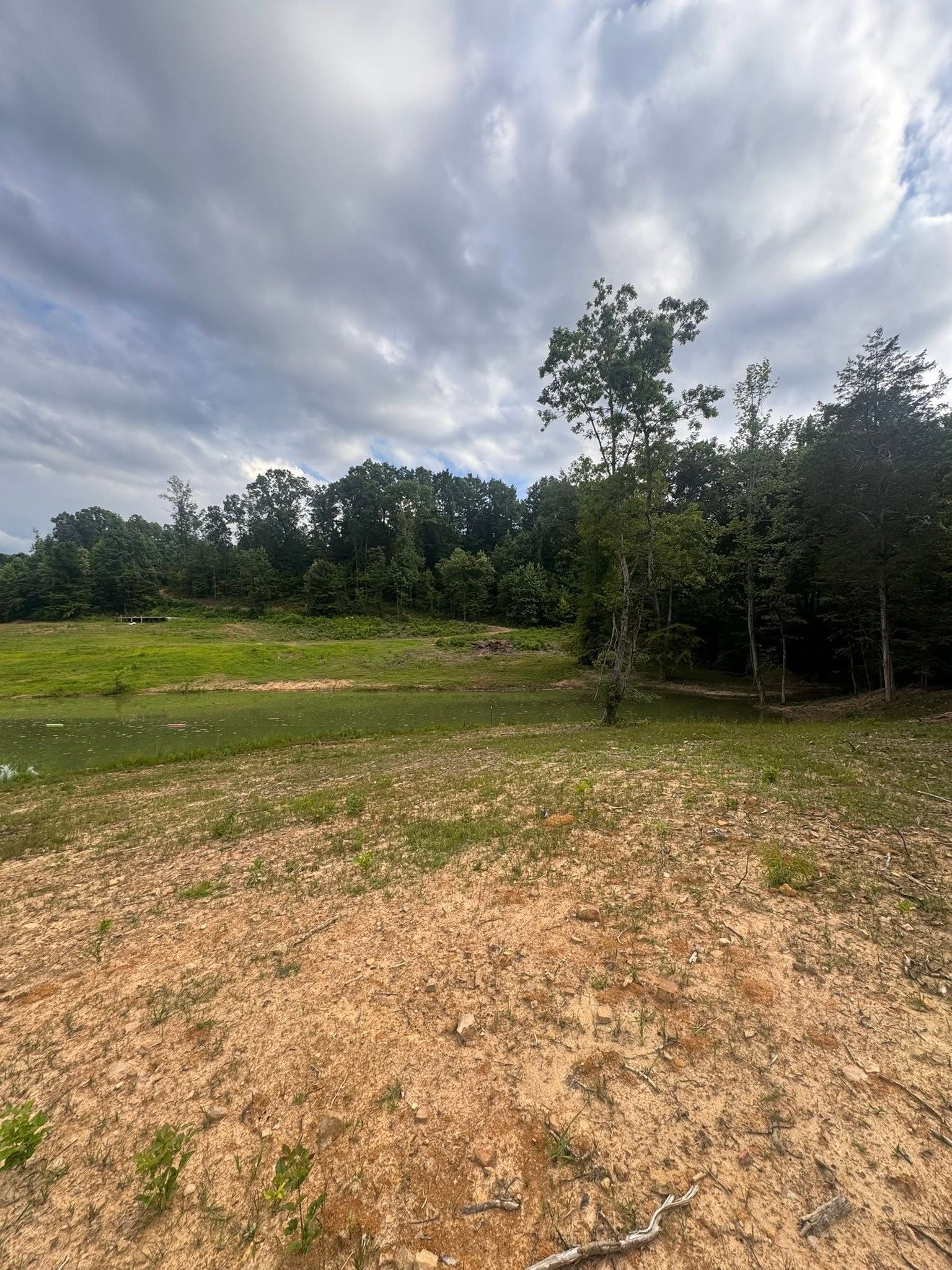 Gravel foreground with grassy field, trees, and a cloudy sky overhead