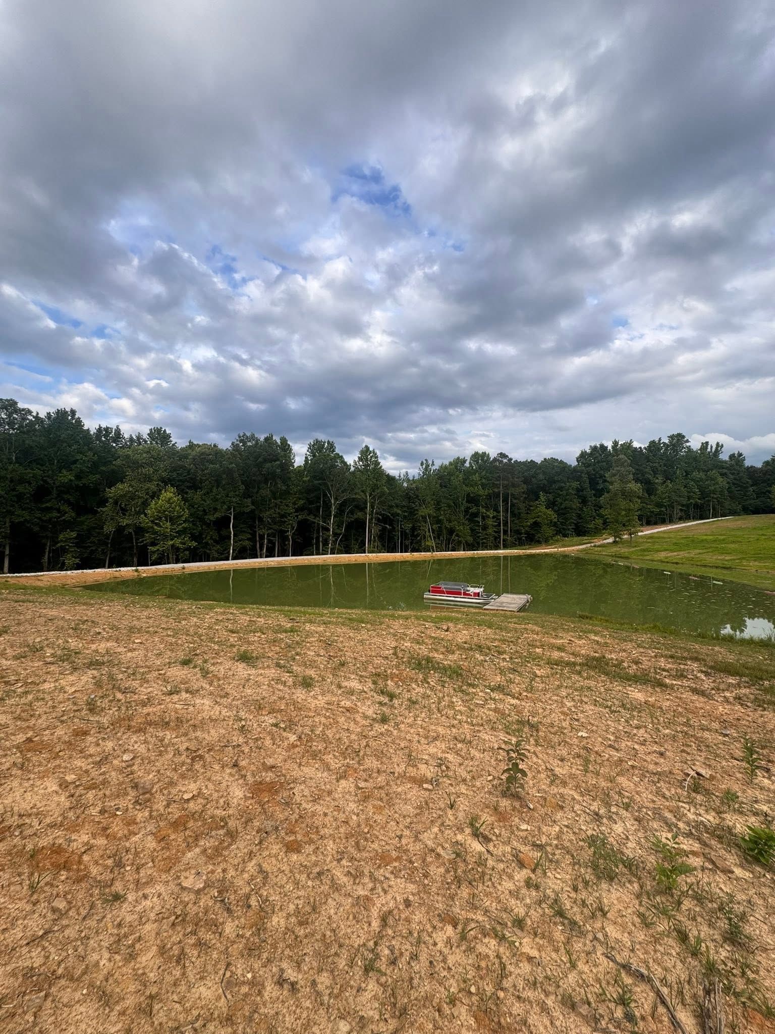 Dry grassy field under a cloudy sky, with a small red-and-white object near a tree line.
