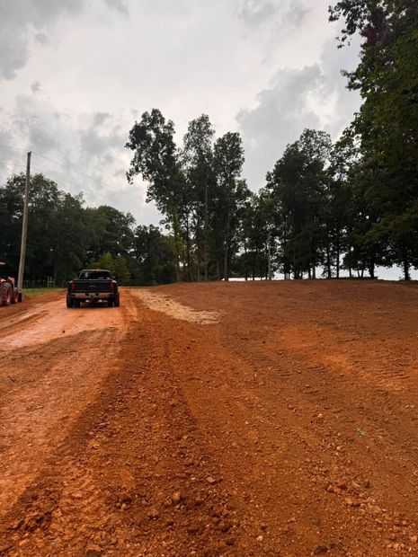 Black car on a muddy dirt road beside trees under a cloudy sky