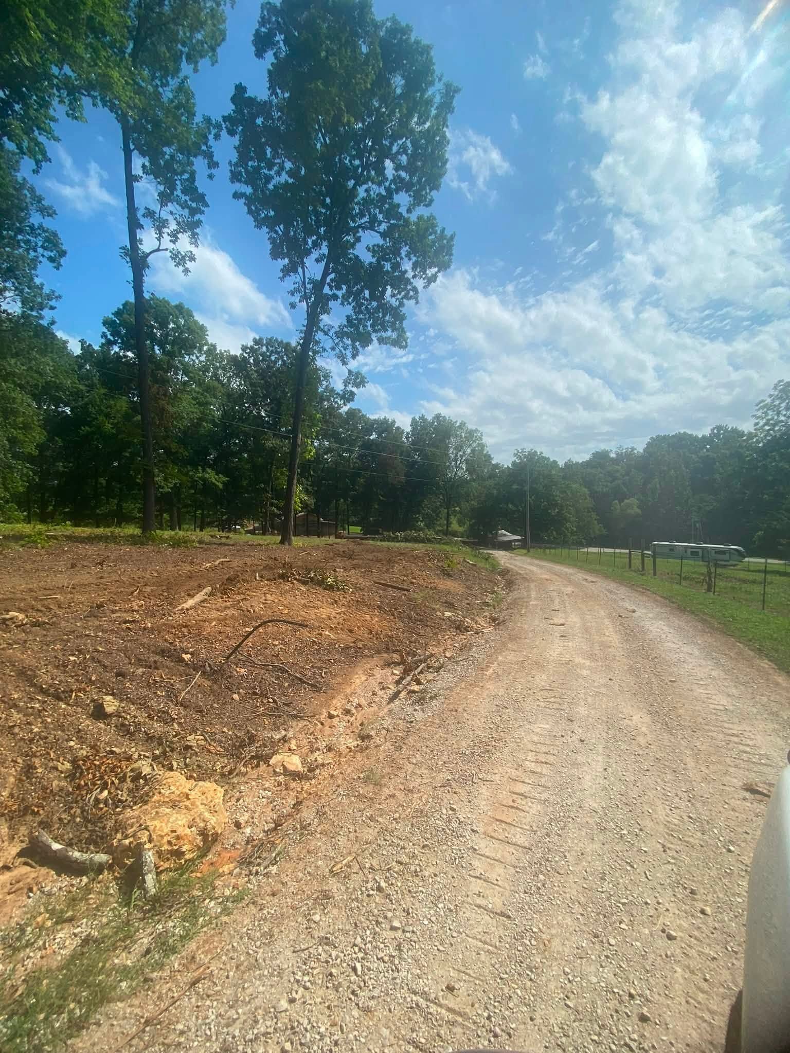 Gravel road curving through a cleared wooded area under a bright blue sky with scattered clouds