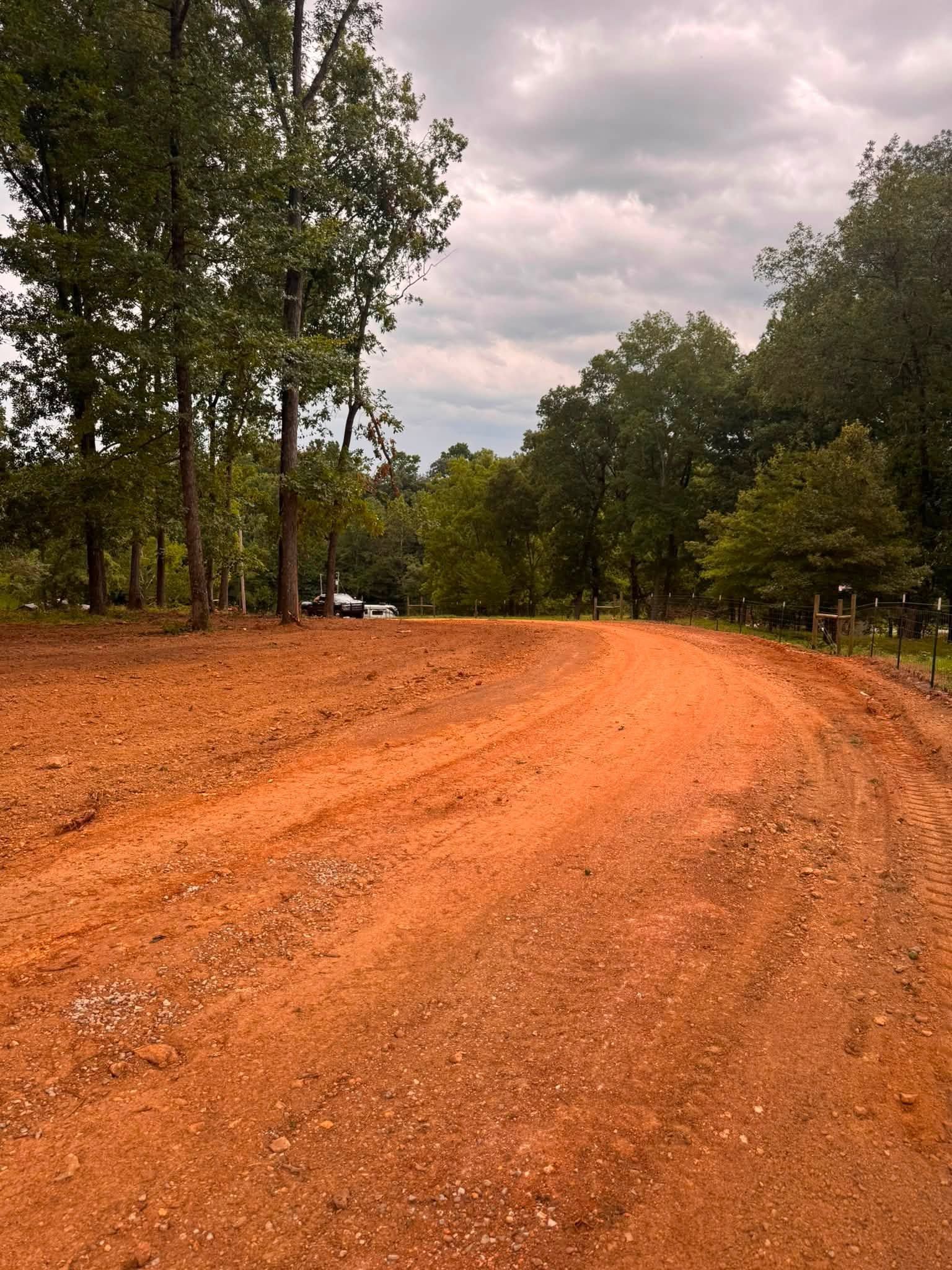 Curving orange dirt road through trees under a cloudy sky