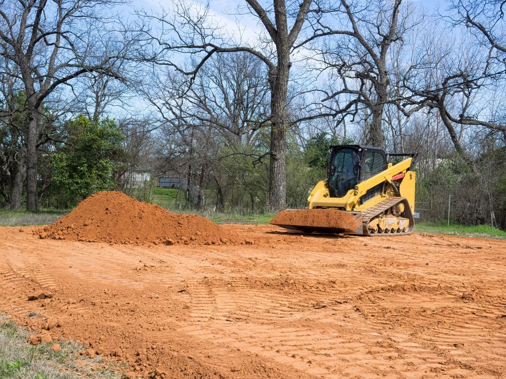 Yellow bulldozer leveling dirt near a mound in a bare wooded construction site