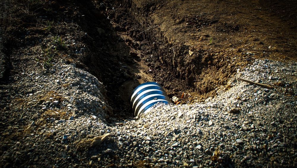 Blue-and-white striped pipe protruding from a rocky dirt trench, likely drainage or utility work
