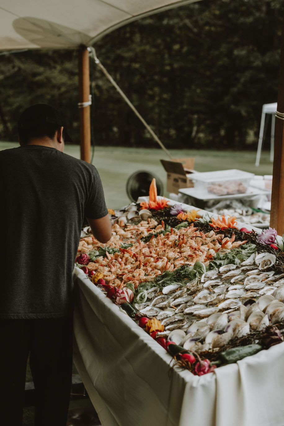 A man is standing in front of a table filled with shrimp and oysters.