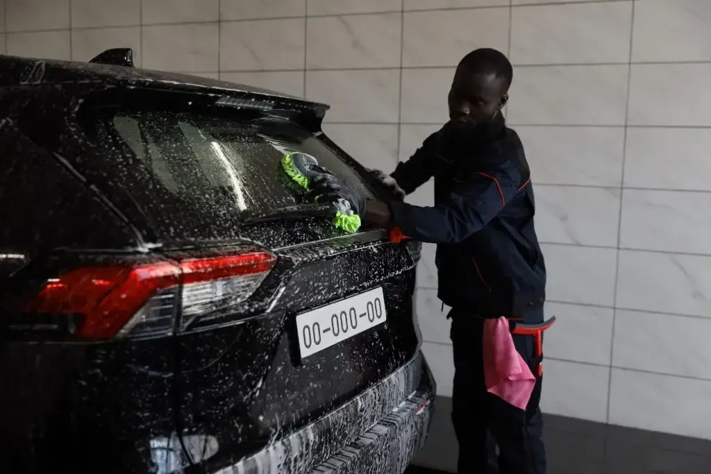 A man is washing a black car in a car wash.