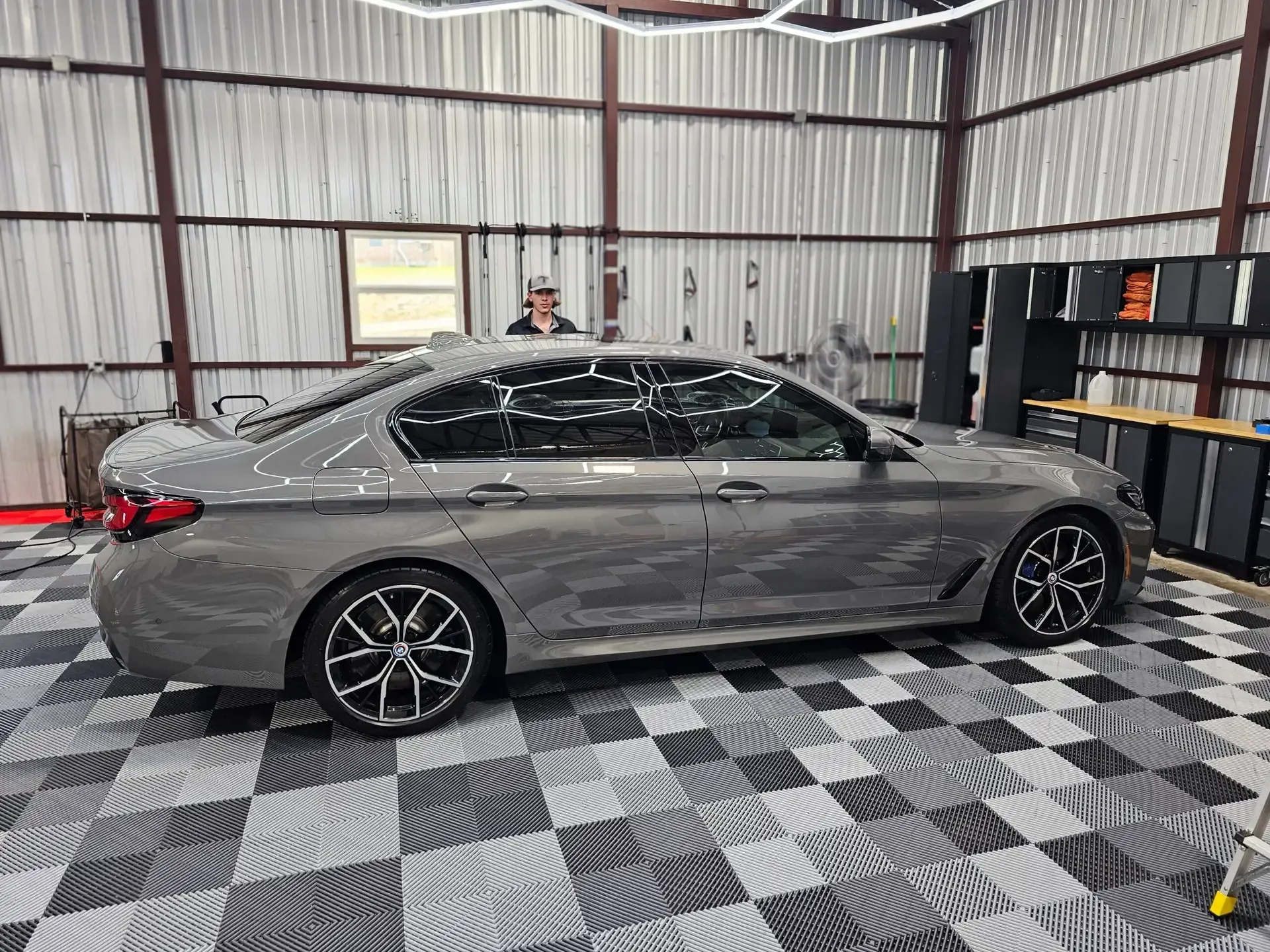 A gray car is parked in a garage with a checkered floor.