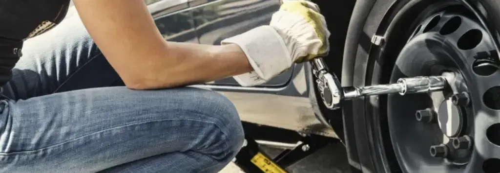 A woman is kneeling down to change a tire on a car