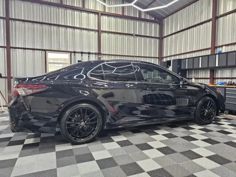 A black car is parked in a garage with a checkered floor.