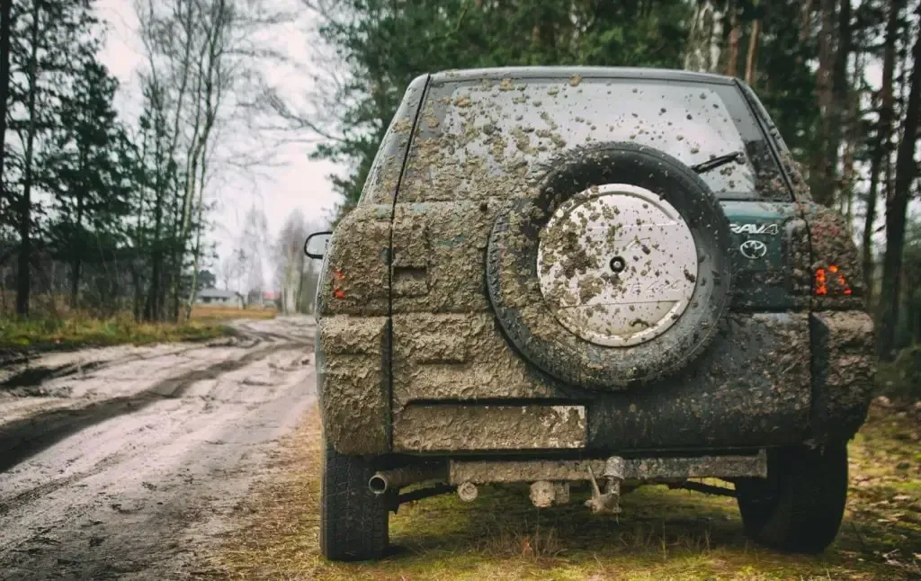 A muddy suv is parked on the side of a dirt road.