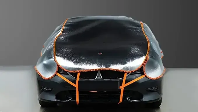 A black car is covered in a clear plastic cover.