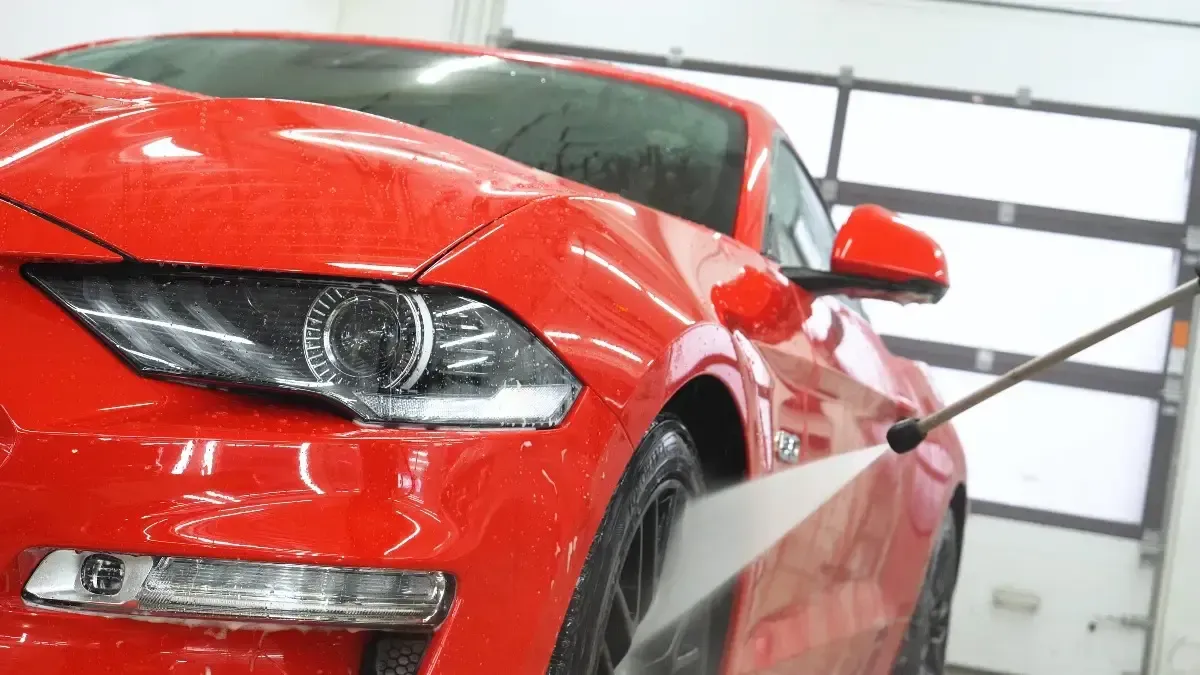 A red mustang is being washed with a high pressure washer.