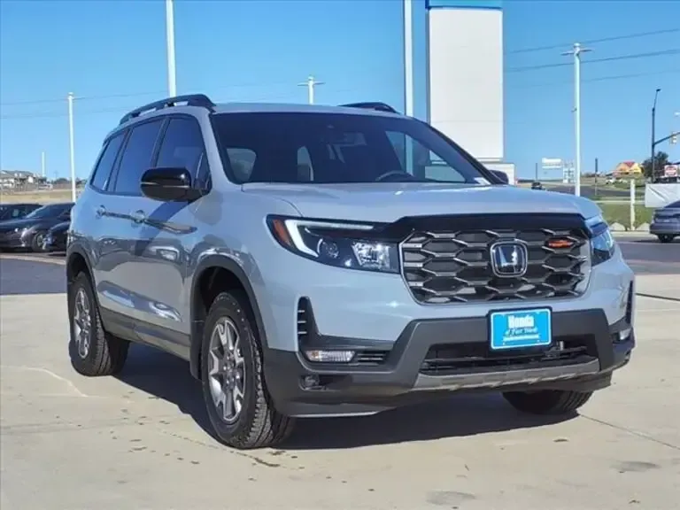 A silver honda passport is parked in a parking lot.