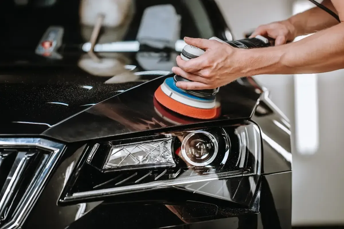 A person is polishing a black car with a machine.