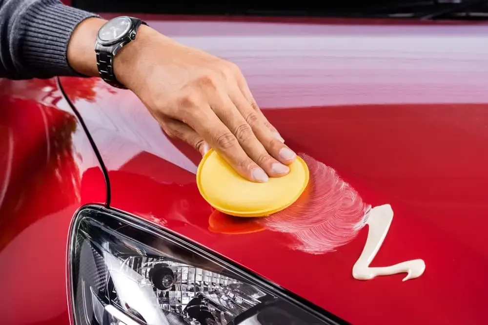 A person is polishing a red car with a yellow sponge.