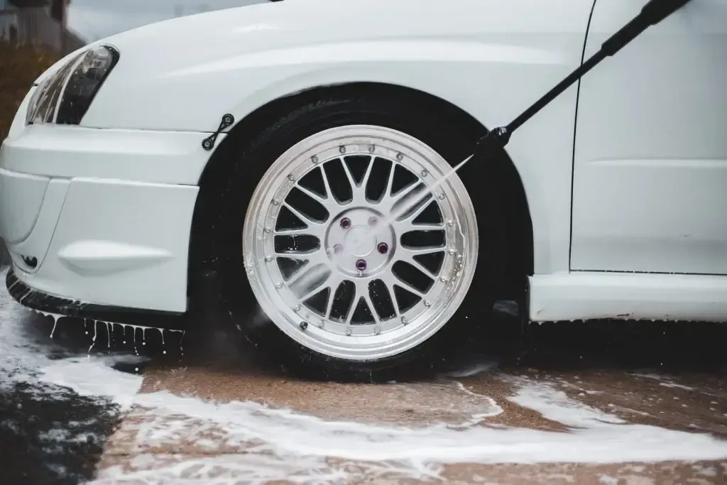 A white car is being washed with a high pressure washer.