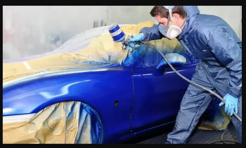 Two men are spray painting a blue car in a garage.