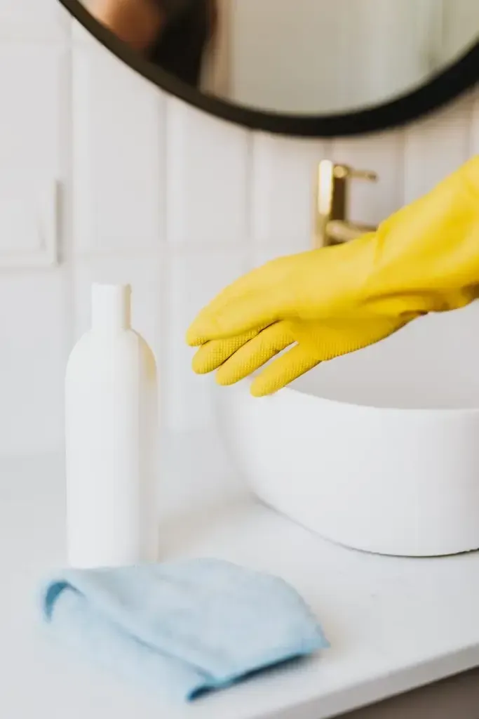 A person wearing yellow rubber gloves is cleaning a bathroom sink.