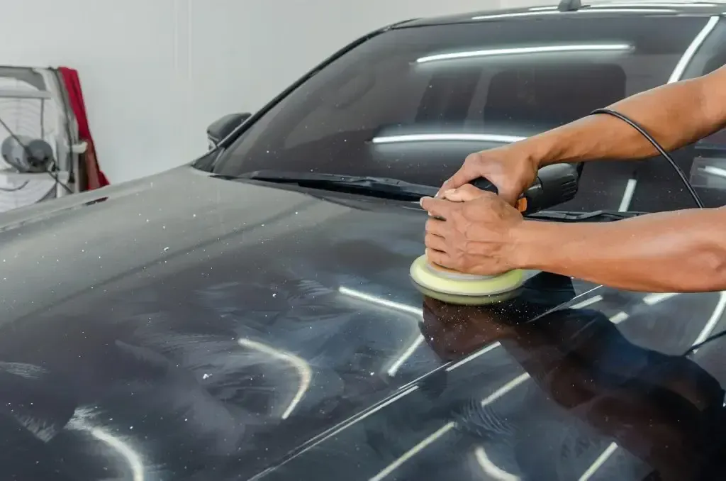 A man is polishing the hood of a black car.
