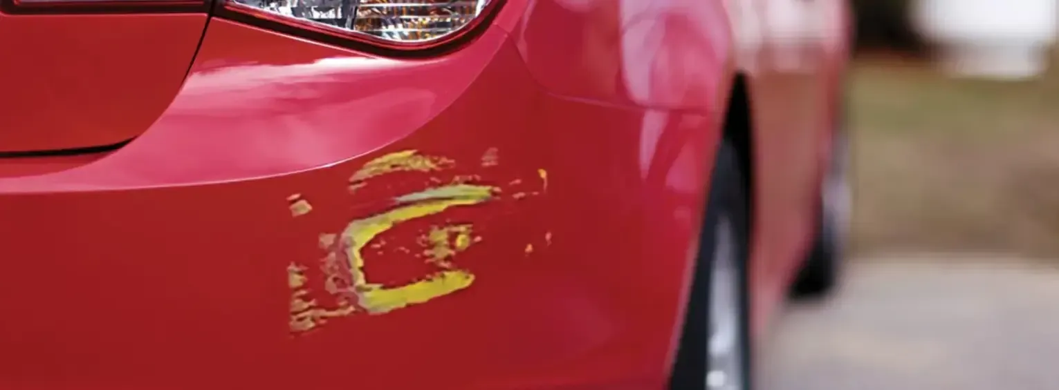 A red car with a damaged bumper is parked on the side of the road.