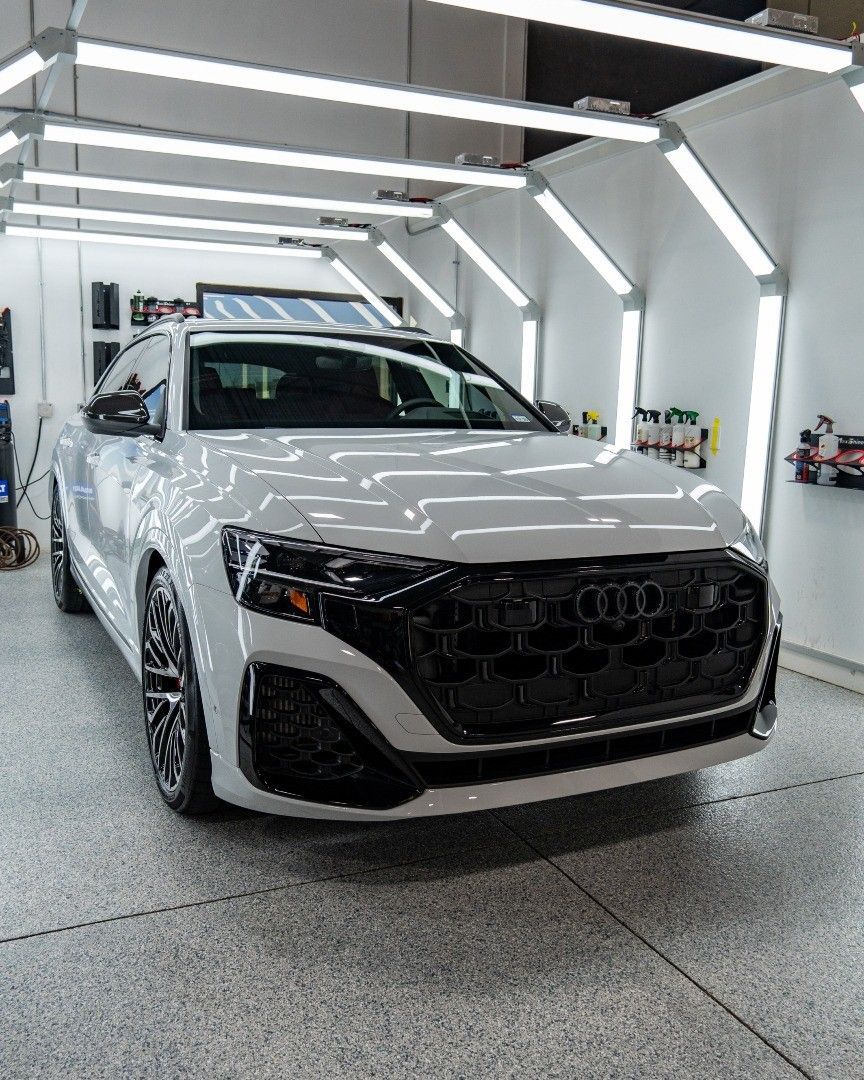 White Audi Q8 SUV parked in a brightly lit detail shop, with a black grille.