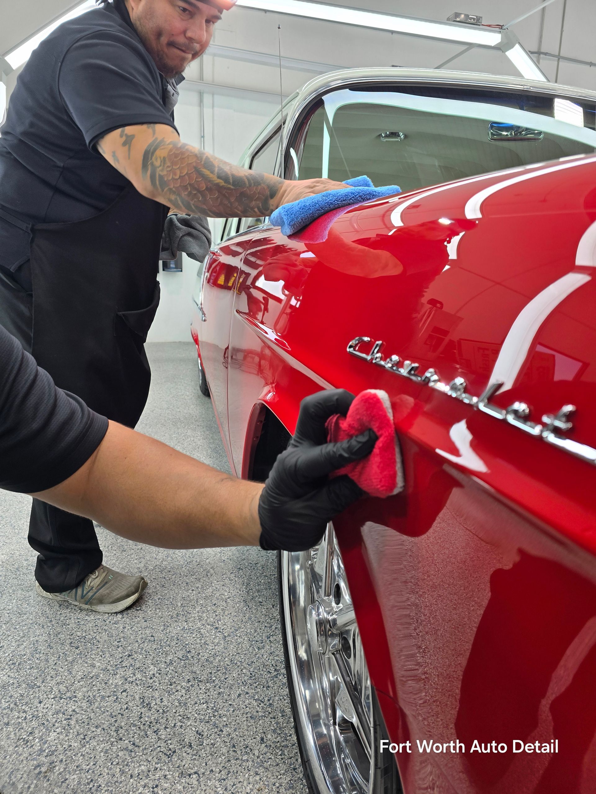 A man with a tattoo on his arm is cleaning a car with a sponge